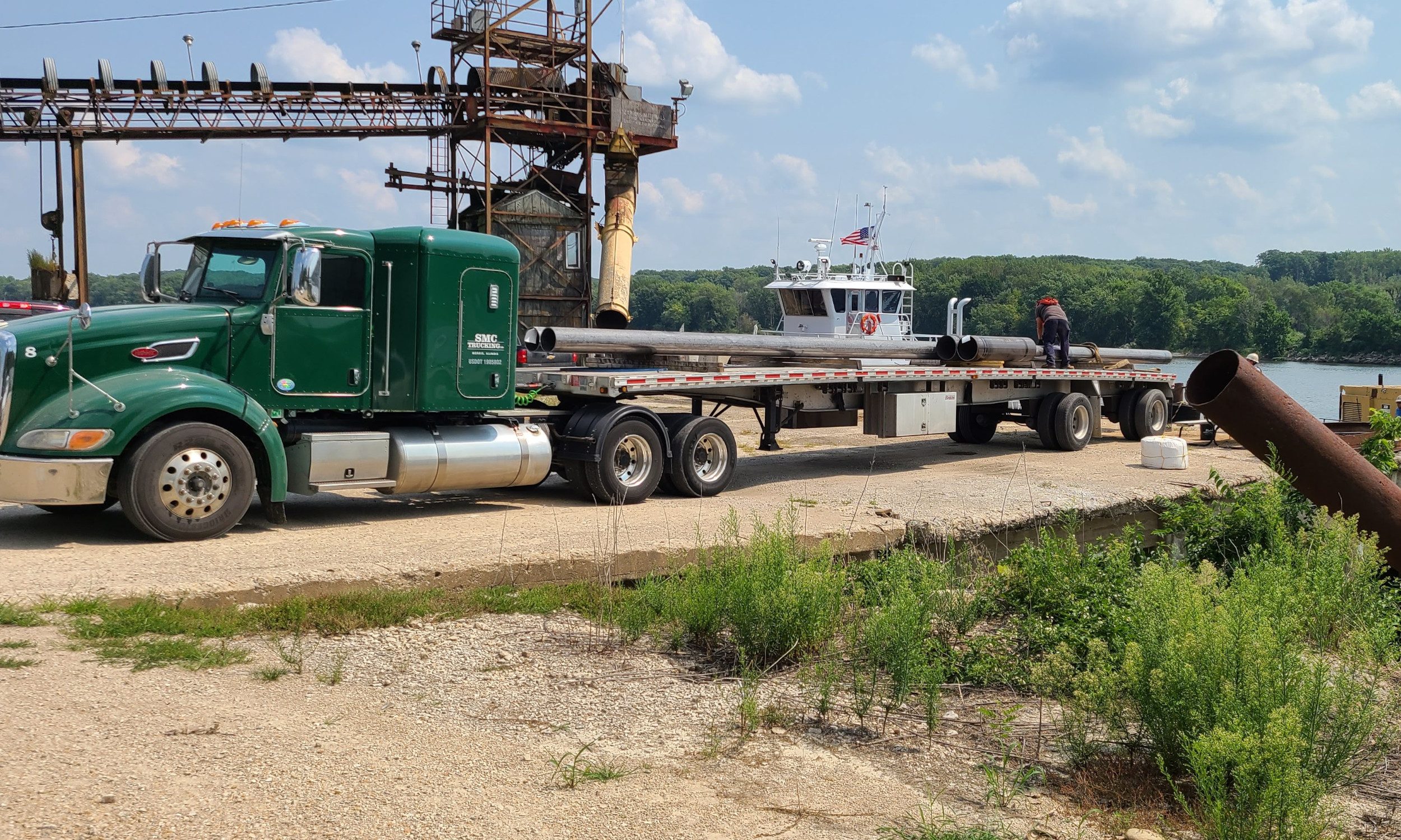 Green Peterbilt unloading Pipe at Barge